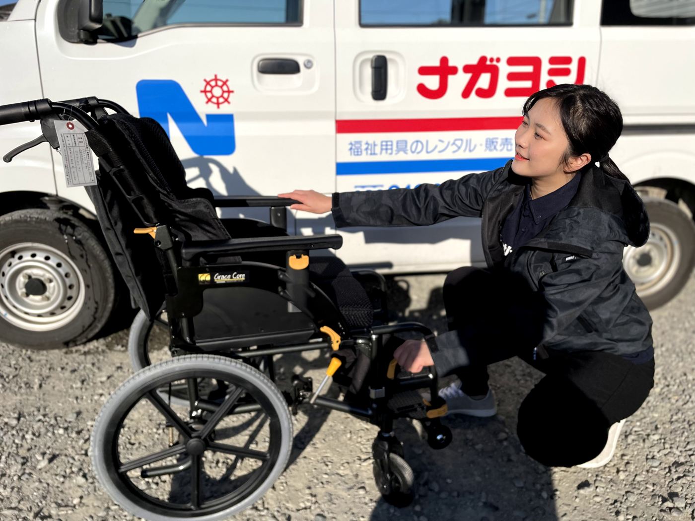 社名入りの車の前で車いすを整える相談員